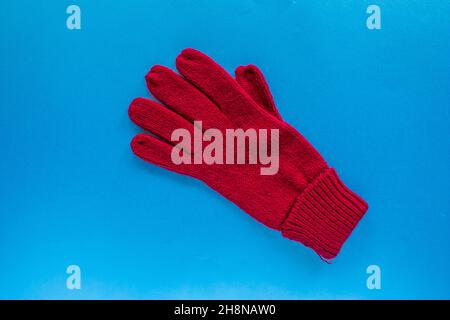 Gant en laine rouge, vue de dessus du gant rouge isolé sur fond bleu. Banque D'Images