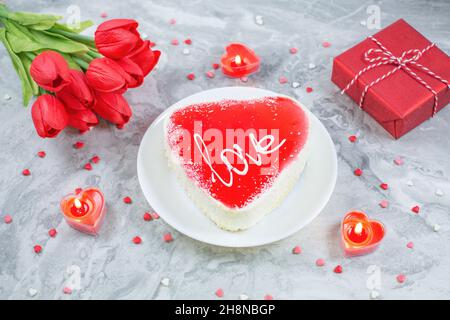 Gâteau en forme de coeur entouré de bougies, boîte cadeau et fleurs sur fond de marbre festif.Concept de la Saint-Valentin. Banque D'Images