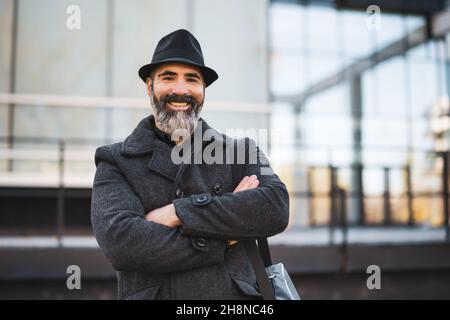 Portrait d'un homme d'affaires heureux vêque de vêtements noirs devant le bâtiment de l'entreprise.L'homme à barbe noire porte des vêtements d'hiver et sourit. Banque D'Images