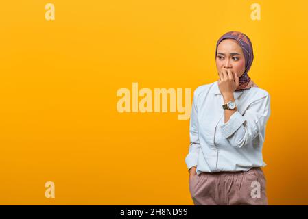 Belle femme asiatique qui a l'air stressée et nerveuse avec des ongles mordant sur fond jaune Banque D'Images