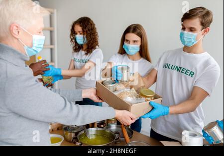 Groupe de jeunes volontaires dans des masques donnant de la nourriture dans des boîtes en carton comme don pour les pauvres et les personnes âgées Banque D'Images