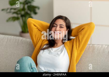 Week-end à la maison.Femme arabe détendue se penchée sur un canapé, reposant sur un canapé confortable avec les mains derrière la tête Banque D'Images