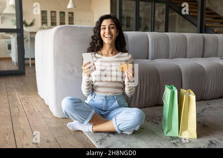 Femme du Caucase du millénaire achetant des biens sur Internet, en utilisant un smartphone et une carte de crédit à la maison, espace libre Banque D'Images
