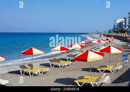 RHODES, GRÈCE - 15 septembre 2021 : chaises longues avec parasols rouges et jaunes sur la plage Akti Kanari à Rhodes, Grèce Banque D'Images