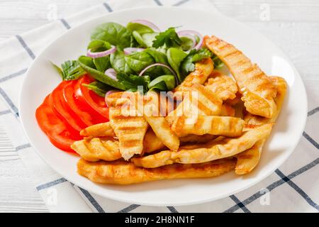 lanières de poulet grillées sur une assiette blanche avec des épinards frais crus, des oignons rouges et des tomates, un régime de keto friendly, une recette américaine, gros plan Banque D'Images