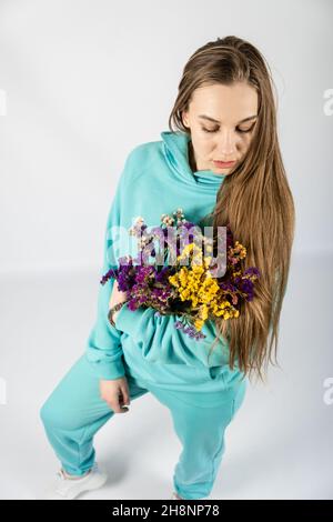 Portrait émotionnel candide de jeune femme blonde heureux à cheveux longs avec bouquet de fleurs sur fond clair. Banque D'Images