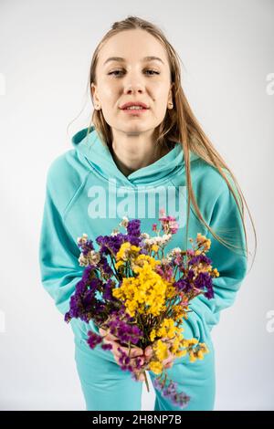 Portrait émotionnel candide de jeune femme blonde heureux à cheveux longs avec bouquet de fleurs sur fond clair. Banque D'Images