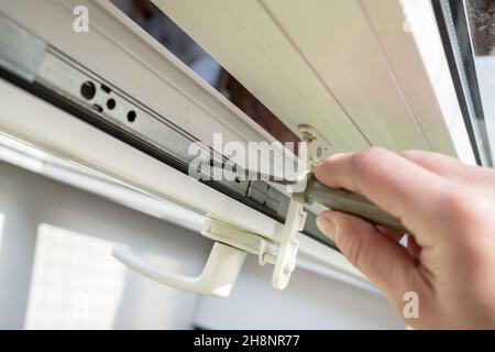 Femme main avec un tournevis règle les raccords métalliques sur une fenêtre en PVC blanc en lumière naturelle.Vue de dessus. Banque D'Images