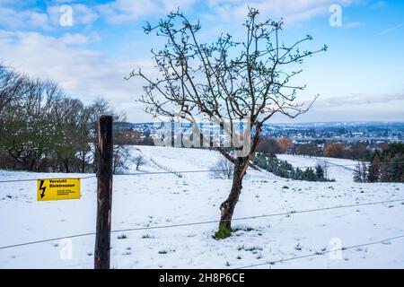 Panneau avec texte allemand 'attention Electric Fence' en face d'un beau paysage d'hiver enneigé avec ciel bleu et quelques nuages.Une petite ville à l'arrière Banque D'Images