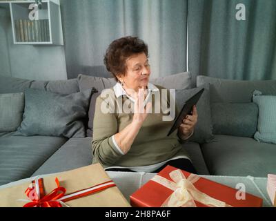 Une femme âgée empaquit des cadeaux et tient une tablette dans ses mains Banque D'Images