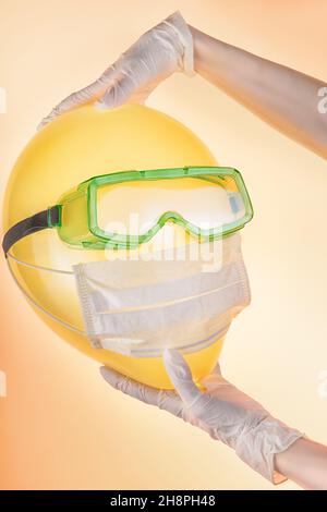 Femme mains dans des gants de protection tenant un ballon dans des lunettes de sécurité et un masque médical.Sécurité, protection pendant l'épidémie de COVID-19 et le thème de verrouillage Banque D'Images