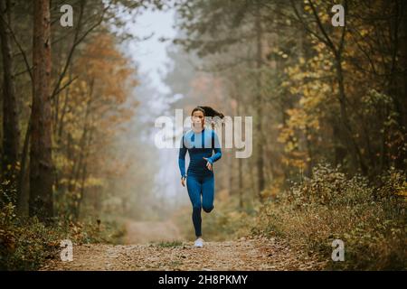 Jeune femme en costume bleu de course vers la caméra sur le sentier forestier à l'automne Banque D'Images