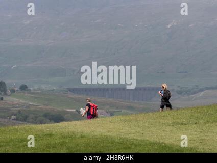 Deux marcheurs sur les trois pics de sentier se sont fortement concentrés sur un foyer doux, la chaleur de toile de fond loin de la colline de Whernside et le viaduc de Ribblehead. Banque D'Images