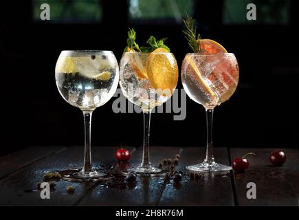 Variedades de bebida alcohólica (tragos de gin et tonique) con limón, pomelo, naranja y hielo en rústica mesa de madera mojada, adorerto con cerezas. Banque D'Images