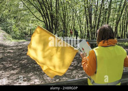 Vue arrière d'un responsable de course agitant un drapeau jaune et prenant des notes pendant un rallye.Concept de voitures de course, de sports automobiles, de rallye, d'offroad, de course et de saf Banque D'Images