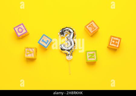Ballon d'argent en forme de figure 3 et cubes en bois avec des lettres sur fond jaune Banque D'Images