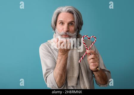 Homme âgé avec des cannes sucrées soufflant baiser sur fond de couleur Banque D'Images