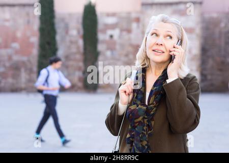 La femelle adulte mesure de parler par téléphone avec ami dans la rue piscine Banque D'Images