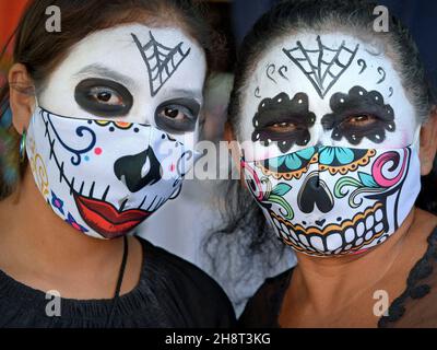 Deux femmes mexicaines à double masque avec maquillage de visage effrayant Catrina le jour des morts portent des masques de visage en tissu imprimé pendant la pandémie de corona. Banque D'Images