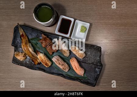 Vue de dessus image de sushi grillé sur une assiette noire avec tasse de thé vert, variété de sushi sains grillés, saumon, thon, crevettes, boeuf et Engawa. Banque D'Images