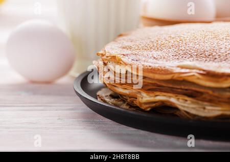 Pile de crêpes françaises dans une poêle sur une table de cuisine en bois avec du lait oeufs et farine de côté Banque D'Images