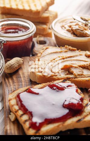 Vue à bas angle sur le beurre d'arachide et les sandwichs de confiture à bord de la planche à découper avec toasts de côté. Concept de saine alimentation Banque D'Images