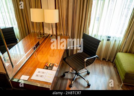 Un espace de travail moderne avec une élégante table en bois, une lampe de table, un grand miroir et un fauteuil noir dans une chambre de luxe. Banque D'Images