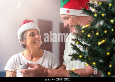 Couple senior regarde l'un l'autre dans l'amour tout en décorant l'arbre de noël Banque D'Images