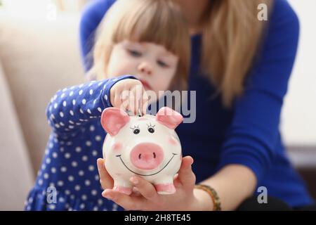 Une petite fille met une pièce de monnaie dans une banque de porc rose Banque D'Images