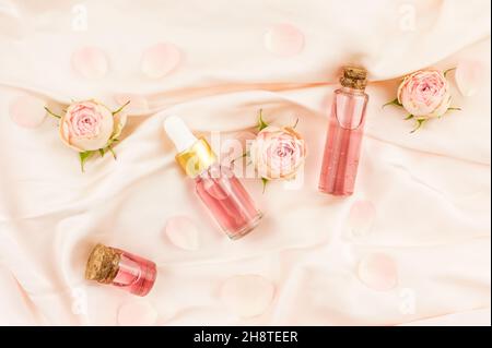 Cosmétiques nature en bouteilles de verre sur fond textile pastel. Eau de rose et huile cosmétique. Vue sur le dessus Banque D'Images