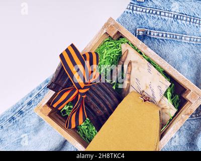 Une boîte avec un ancien magazine pour les cartouches, les cartouches, un ruban St. George est sur les jeans modernes. Banque D'Images