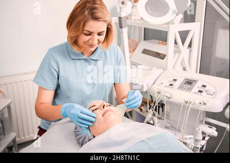 Cosmétologue supprimant le masque de nettoyage en profondeur du visage de la cliente femelle.Jeune femme couché sur un lit de repos tout en ayant une procédure de soin de la peau au centre médical de bien-être.Concept de beauté et de soin du visage. Banque D'Images