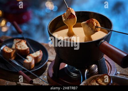 De dessus de délicieux croquants croquant croûtons de pain étant trempés dans le fondue de fromage chaud dans la casserole placée sur la table en bois en hiver Banque D'Images