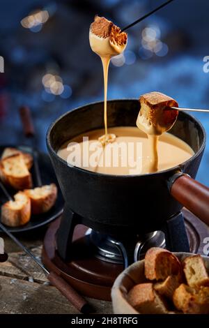 De dessus de croûtons de pain croustillants étant trempés dans du fondue de fromage liquide fondu dans une casserole sur brûleur à gaz en hiver Banque D'Images