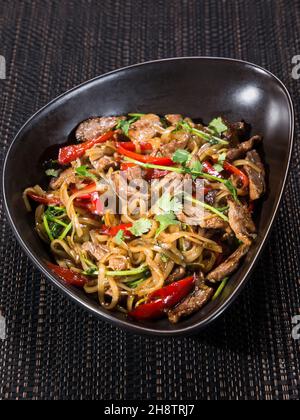 wok, mélanger les nouilles frites avec du bœuf tranché, du poivron et du persil dans la sauce soja, servi dans un bol sur fond sombre, photo verticale Banque D'Images