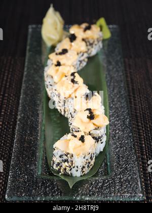 rouette de sushi uramaki aux noix de saint-jacques hachées et au sésame sur fond sombre Banque D'Images