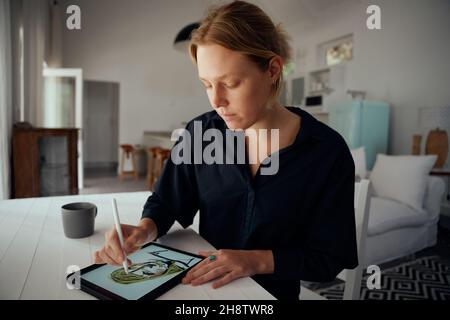 Femme de mode caucasienne assis dans des vêtements de designer de bureau à domicile sur une tablette numérique Banque D'Images