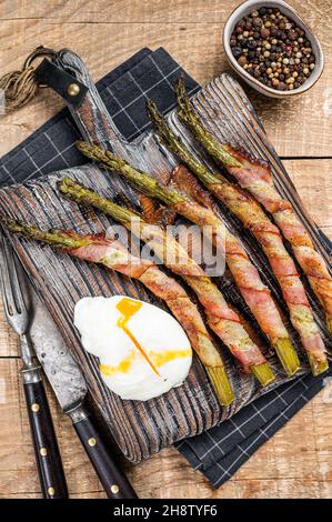 Asperges vertes rôties enveloppées dans un bacon avec des œufs. Arrière-plan en bois. Vue de dessus Banque D'Images