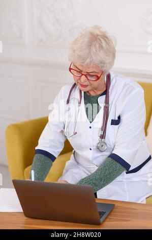 Femme d'âge moyen médecin utilisant un ordinateur portable, écrivant des notes avec le stéthoscope sur la table.Concept de soins de santé.Médecin écrivant et prenant des notes Banque D'Images