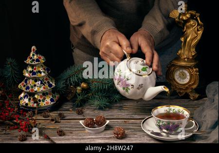 Cérémonie du thé avec théière de Noël et tasse de thé, bonbons dans une plaque en céramique, branches d'arbre de Noël, arbre de Noël en céramique et une horloge antique sur le woo Banque D'Images
