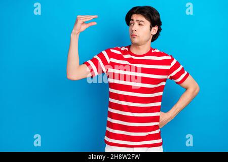 Photo de douteux drôle jeune homme porter t-shirt rayé mesurer les doigts petit espace vide isolé couleur bleu fond Banque D'Images