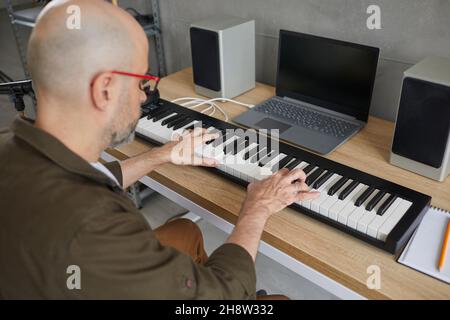 Homme qui aime jouer de la musique joue sur un synthétiseur moderne créant une nouvelle composition musicale. Banque D'Images