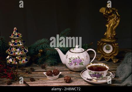 Théière et tasse de thé de Noël spectaculaires, bonbons dans une assiette en céramique, branches d'arbre de Noël, arbre de Noël en céramique et une horloge antique sur une ta en bois Banque D'Images