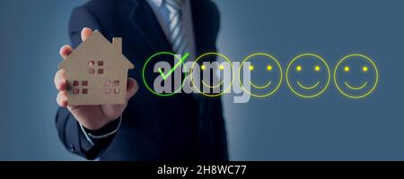 homme d'affaires tenant immobilier petit modèle de bois avec signe de service de pari de sourire Banque D'Images