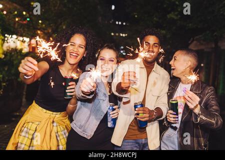 Amis célébrant la veille du nouvel an avec des lumières bengale.Quatre jeunes heureux tenant leurs étincelants à minuit.Groupe d'amis joyeux de la ville Banque D'Images