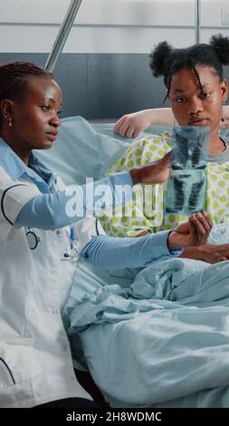 Médecin montrant les résultats de la radiographie à une femme malade au lit.Un spécialiste médical explique le diagnostic de radiographie à un jeune adulte atteint d'une maladie.Médecin parlant au patient dans la salle d'hôpital Banque D'Images