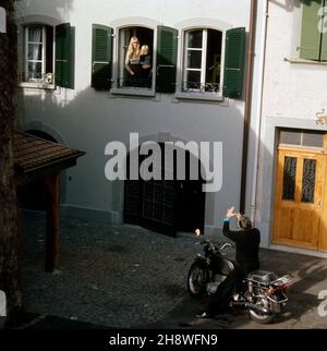 Unternehmer Gunter Sachs macht vom Motorrad aus eine lange Nase zu Ehefrau Mirja und Sohn Christian Gunnar, ca.1974. L'entrepreneur Gunter Sachs montre des mops et des mows à sa femme Mirja et à son fils Christian Gunnar, environ 1974. Banque D'Images