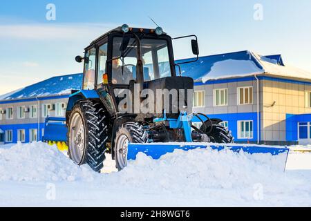 Le tracteur avec pelle dégage de la neige dans les rues.Service de déneigement et de déneigement en hiver.Flux de travail de la scène réelle.Arrière-plan. Banque D'Images