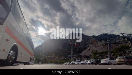 Vue sur la route au rez-de-chaussée d'un autocar touristique de luxe garé dans un parking avec des voitures au-dessous d'un sommet de montagne avec téléphérique au sommet pour visiter Banque D'Images