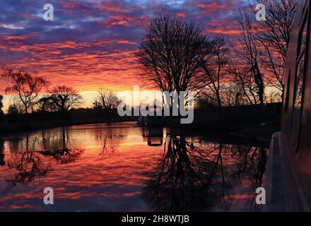 Le soleil brûlant rouge vient de se lever sur un canal froid et glacé de Leeds et Liverpool lors d'une matinée d'automne se reflète le long d'un bateau à rames près de Burscough Banque D'Images
